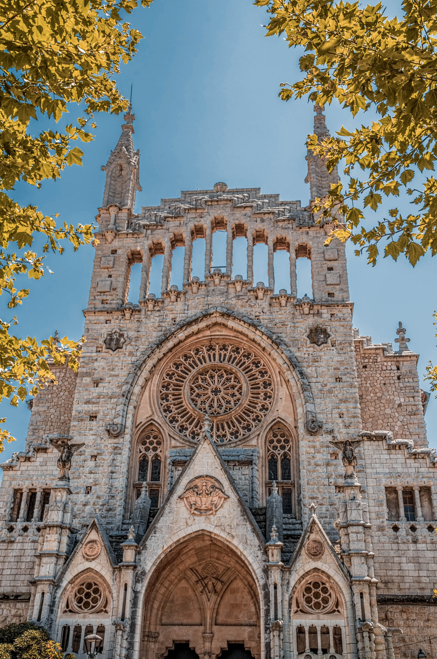 Facade of the Church of Sant Bartomeu in Sóller, Mallorca, featuring its striking modernist architecture with intricate stone details and a large rose window.