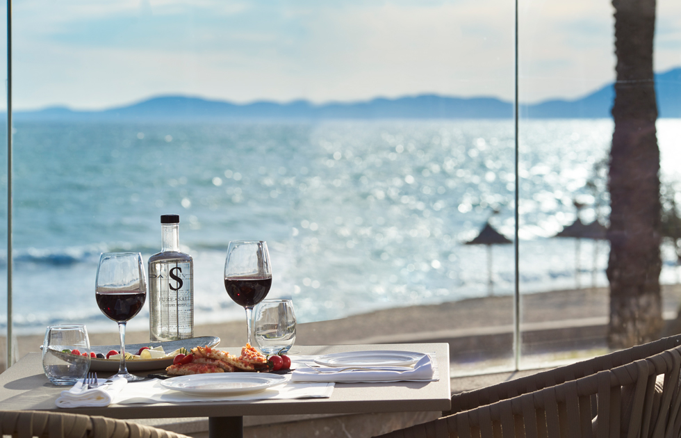 A beautifully set table in the Pure Salt Garonda hotel restaurant, with a Mediterranean dish and a view of the beach through the window.