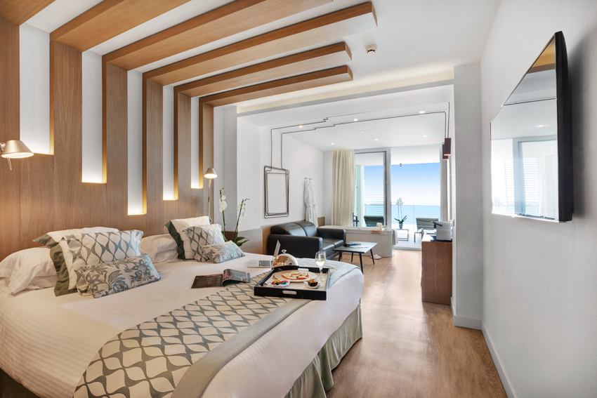 A luxurious hotel room at Pure Salt Garonda with a large bed, modern decor, and a balcony with partial sea views.