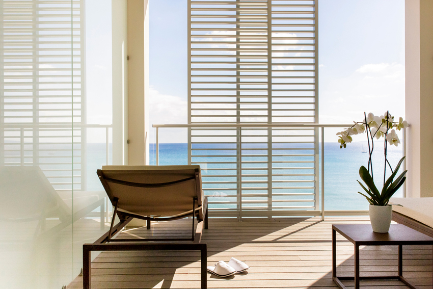 A close-up of a hotel balcony at Pure Salt Garonda, showing the glass railing and the impressive sea view from the room."